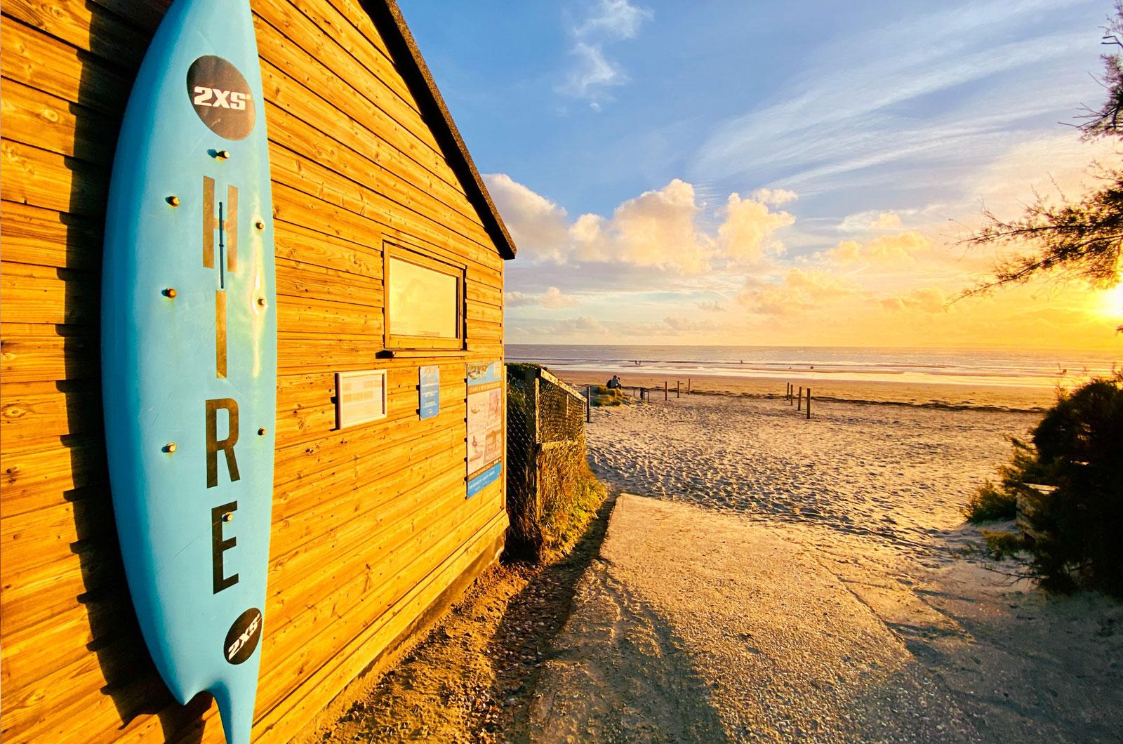 Image of a surfboard with hire written on it and the sea in the background