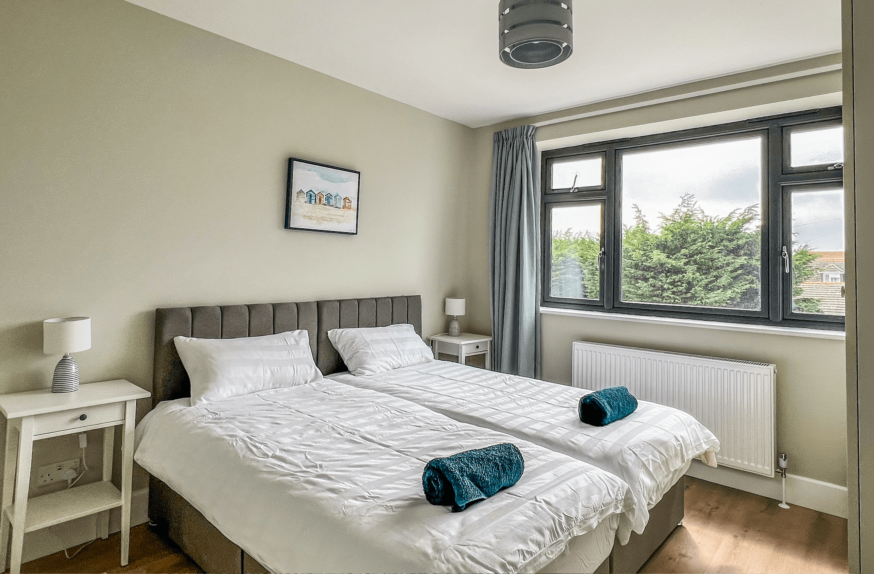 Ocean Grove Image A large double bed sits at the centre of a bedroom. A set of towels are rolled up on the centre of the bed.