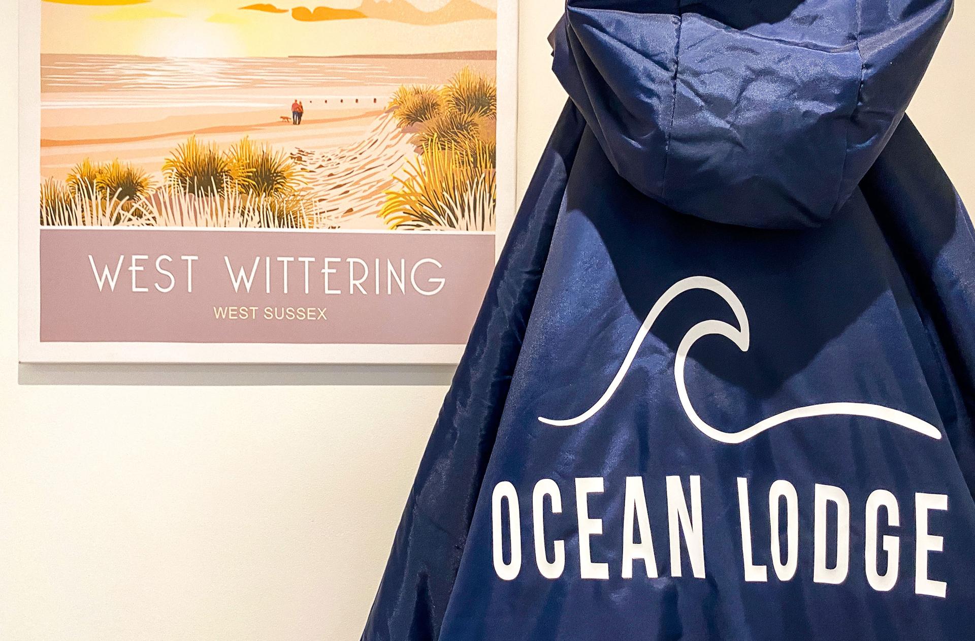 Ocean Lodge Image A West Wittering calendar hands on the wall next to an item of clothing with a hood and the words Ocean Lodge with a wave written above.