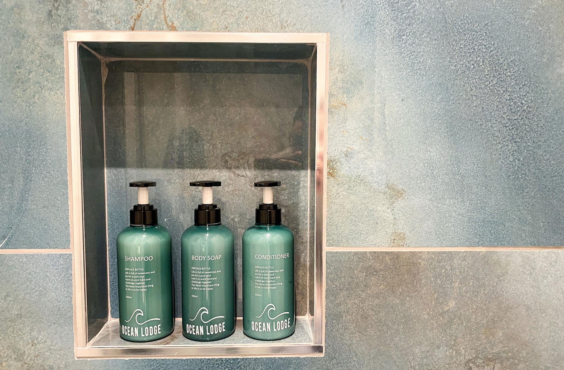 Ocean Lodge Image A set of three shower gels sits in a small alcove in a blue and grey stylised bathroom.