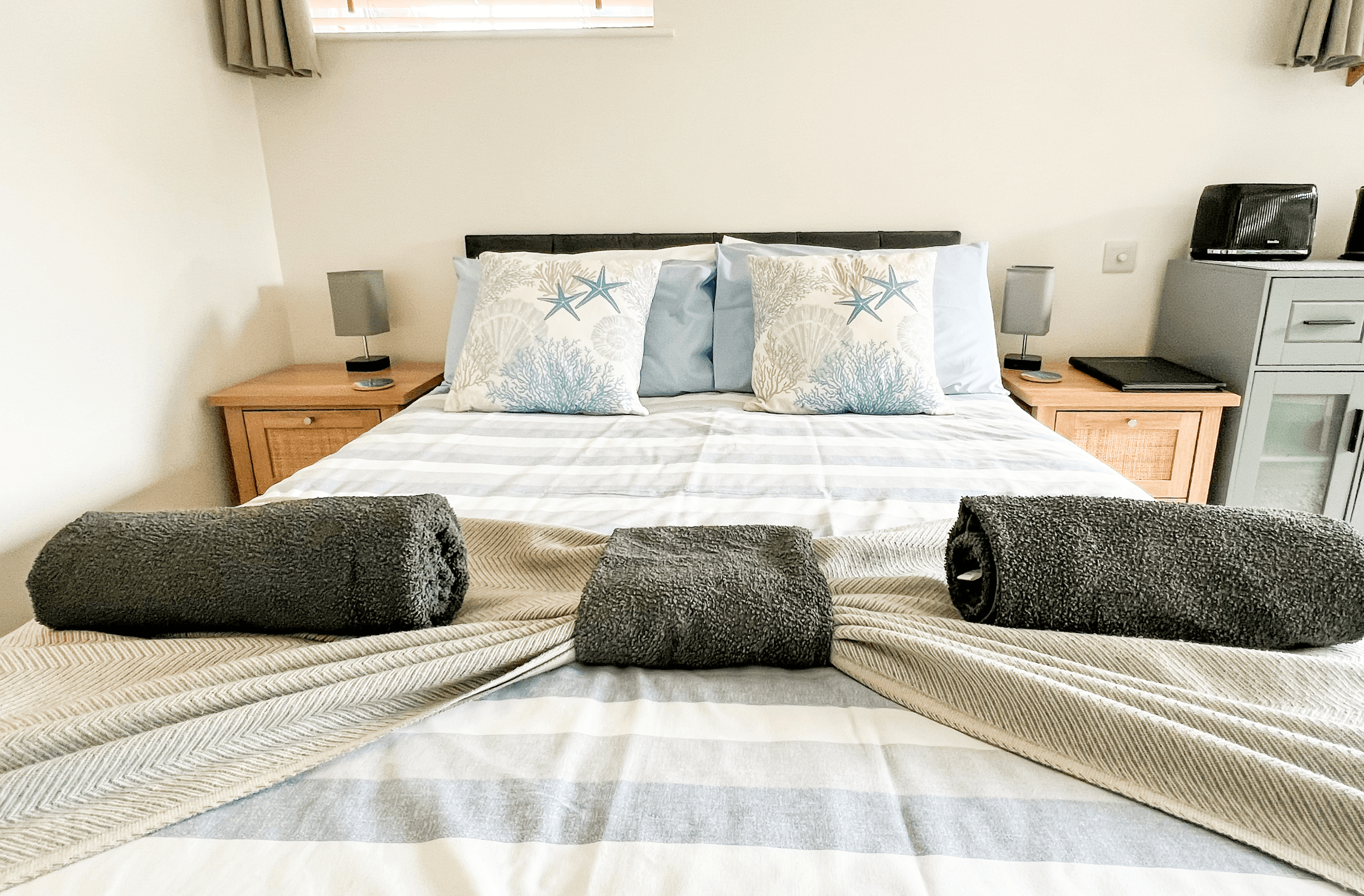 Ocean Lodge Image A set of two pillows and rolled up towels are sitting on a double bed with a surfer feel.