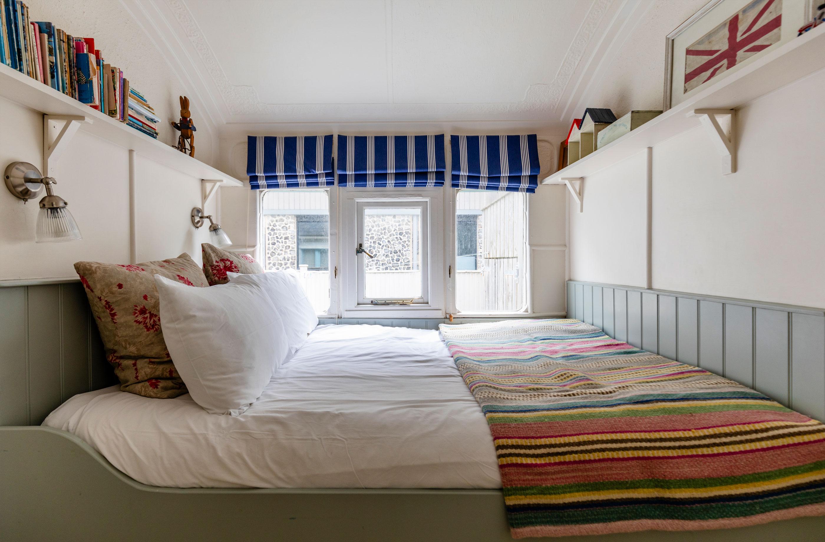 The Dodo Image A comfy double bed with white pillows next to a set of windows at the Dodo property in the Witterings. Blue blinds are opened above the windows.