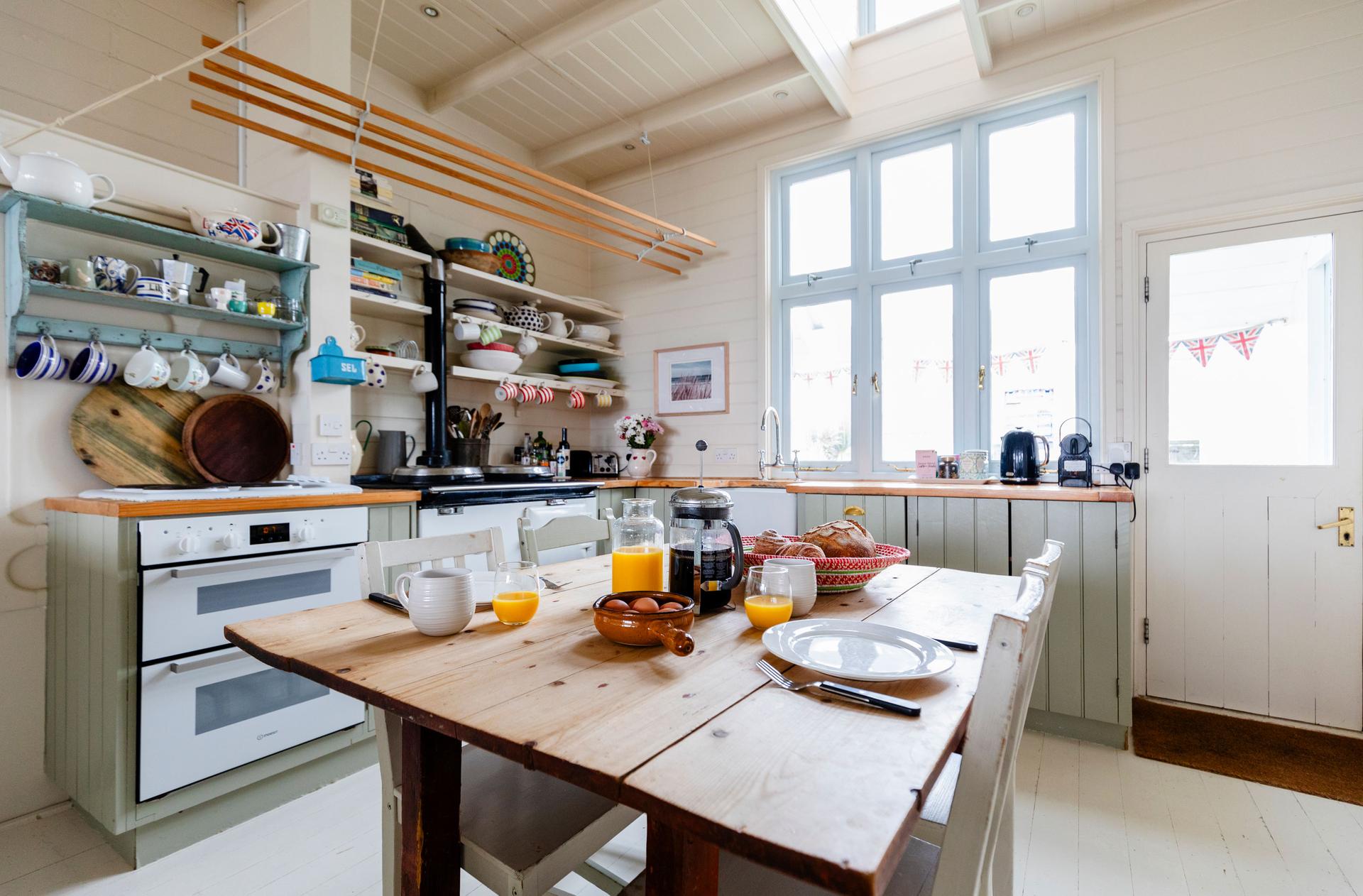 The Dodo Image A view of a kitchen with a table and chairs set with a breakfast. There is a white oven on the left and a door on the right.