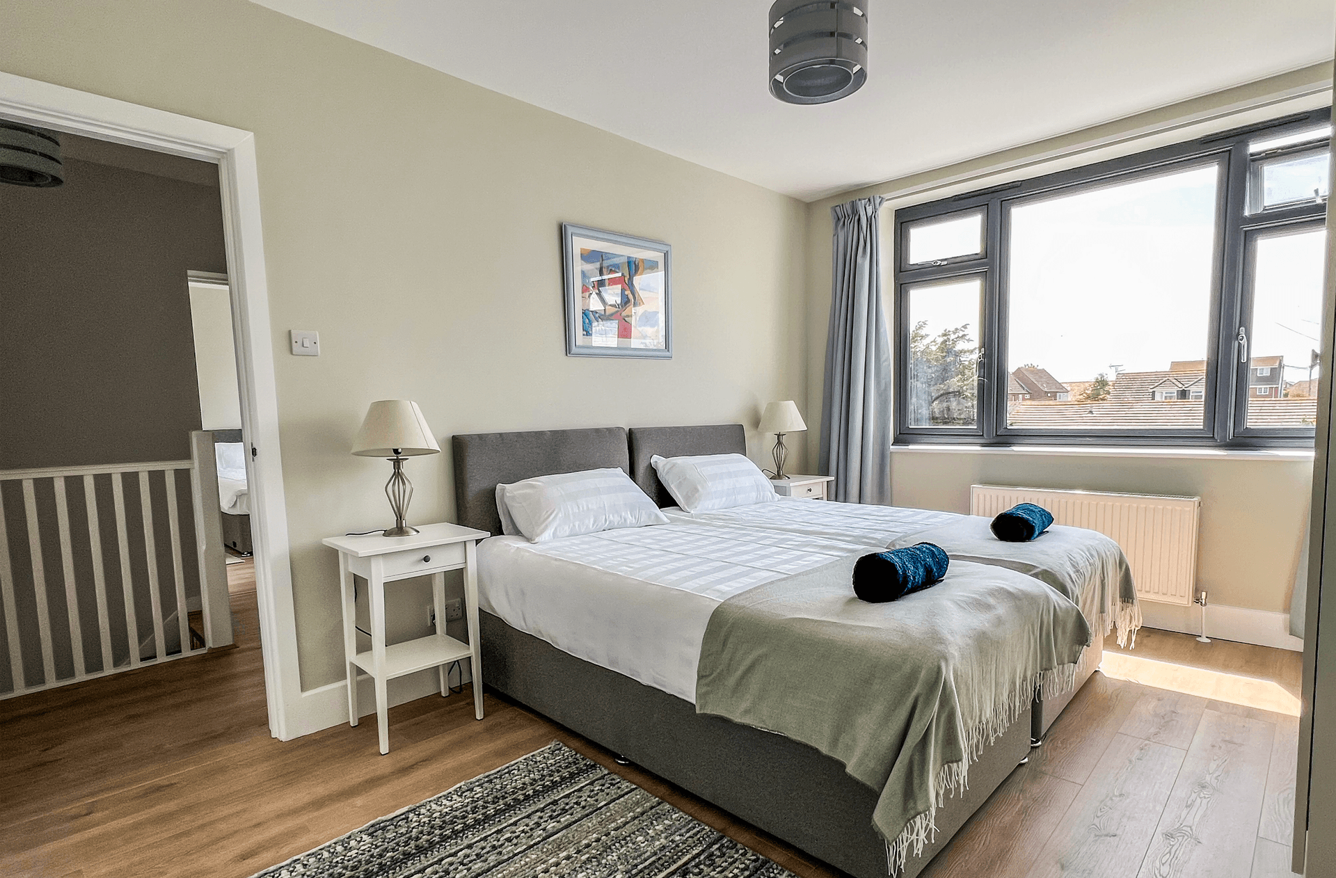 Ocean Grove Image A large double bed sits at the centre of a bedroom. A set of towels are rolled up on the centre of the bed.
