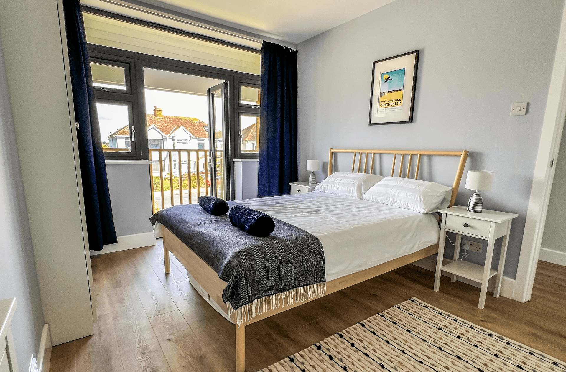 Ocean Grove Image A large double bed sits at the centre of a bedroom. A set of towels are rolled up on the centre of the bed.